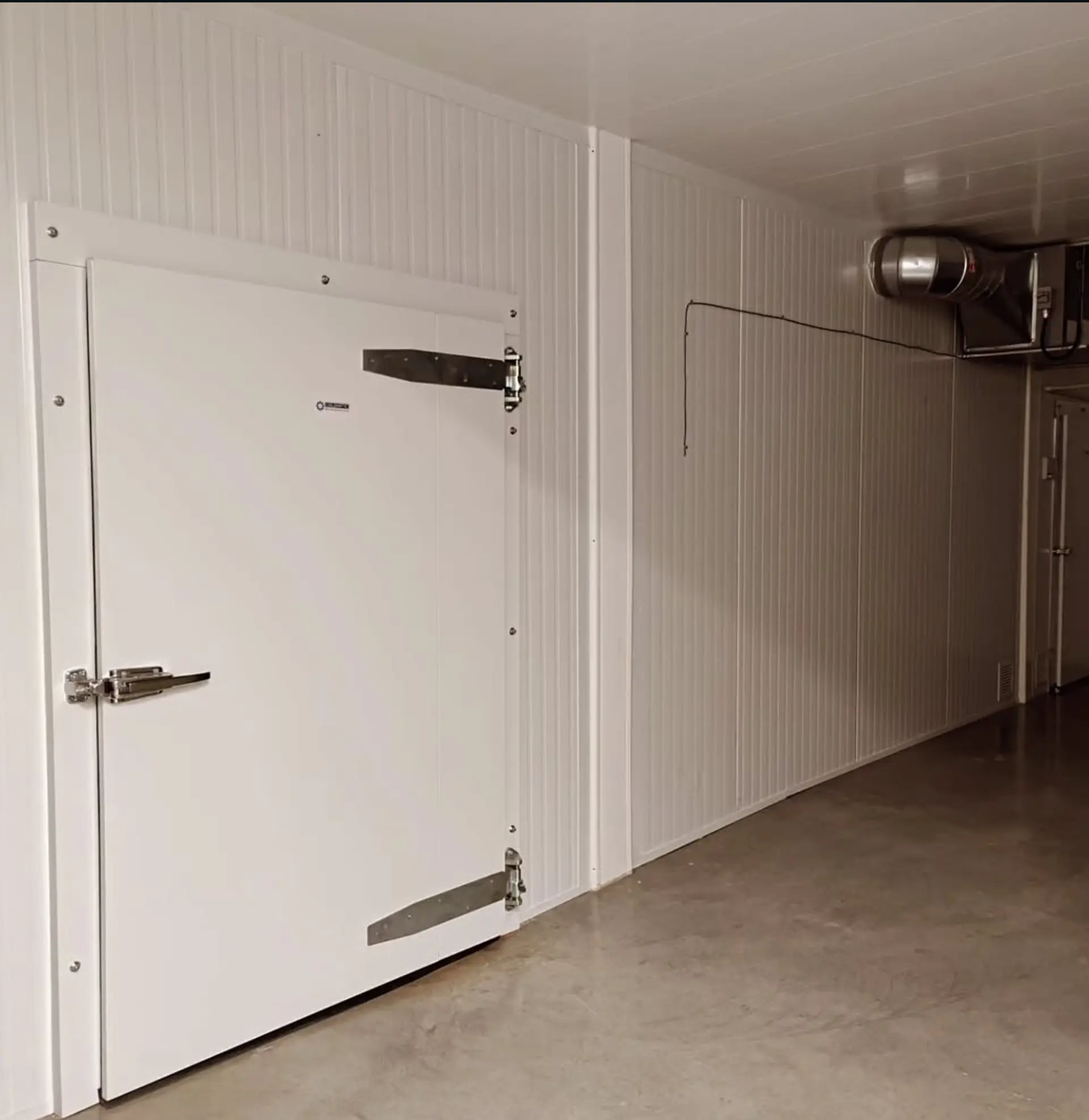 Walk-in cooler door with hinges and latch inside a commercial kitchen